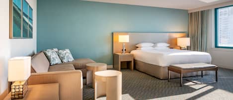 A hotel room with a bed, a sofa, a small table, and a lamp.