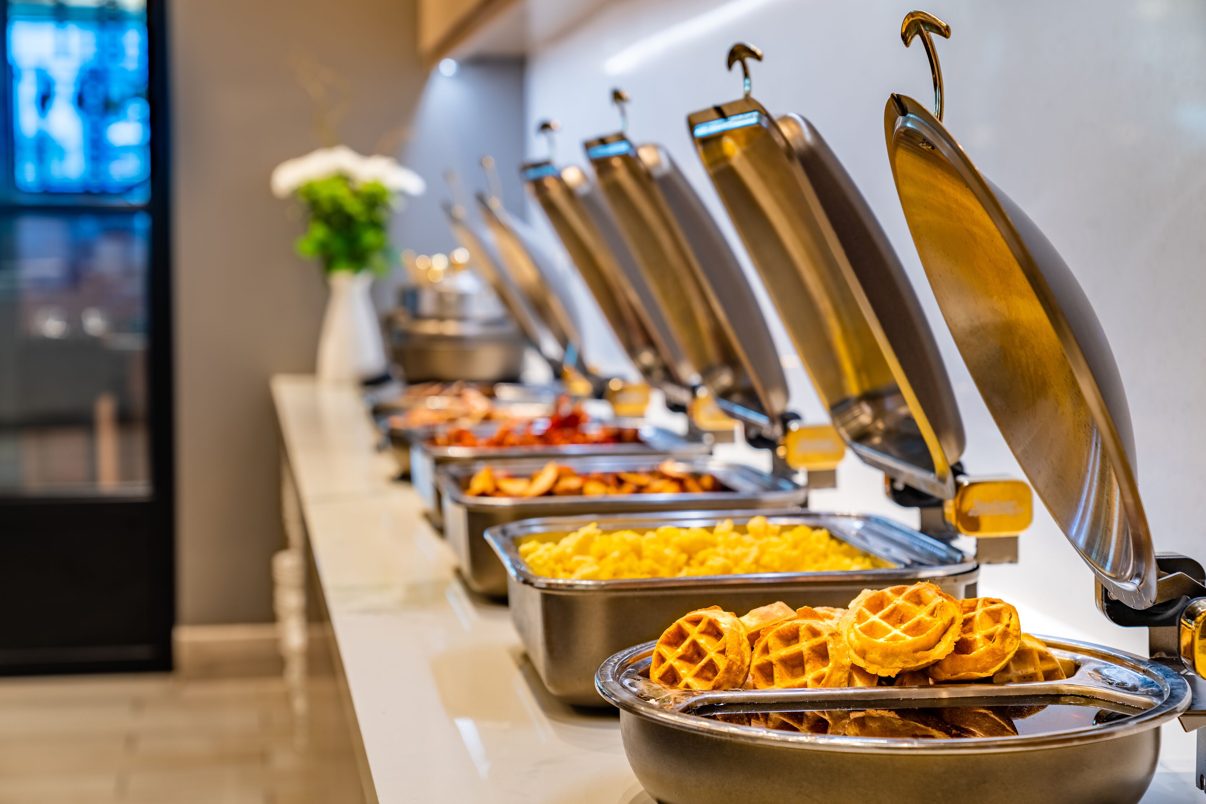 Una barra de buffet con diversos alimentos, incluyendo gofres y otros platos.