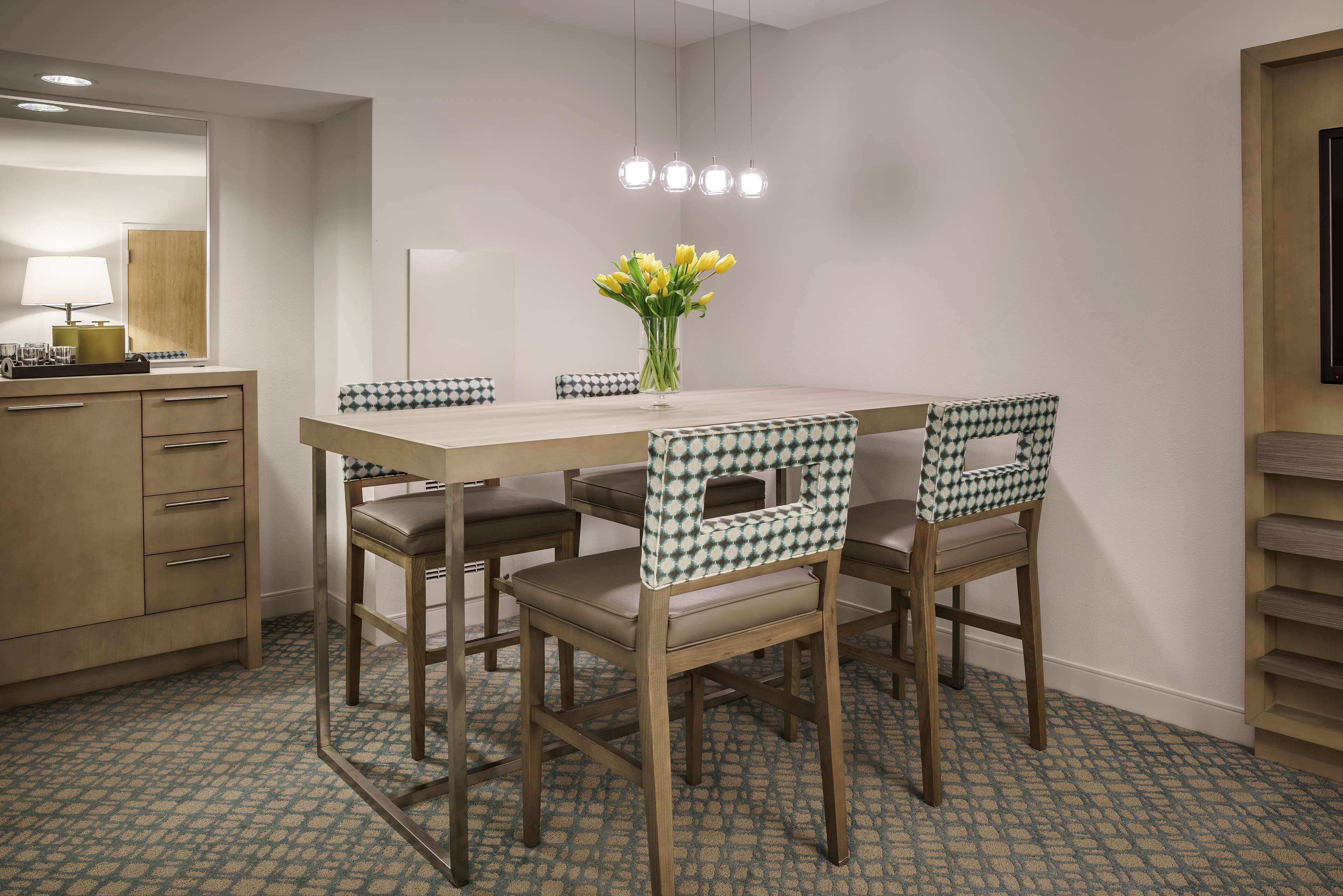 Un comedor con una mesa, sillas, un jarrón de flores y un espejo.