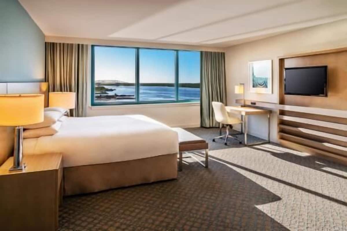 A hotel room with a bed, desk, chair, TV, and a large window with a view.