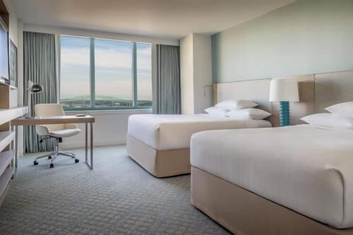 A hotel room with two beds, a desk, a chair, and a view of the landscape.