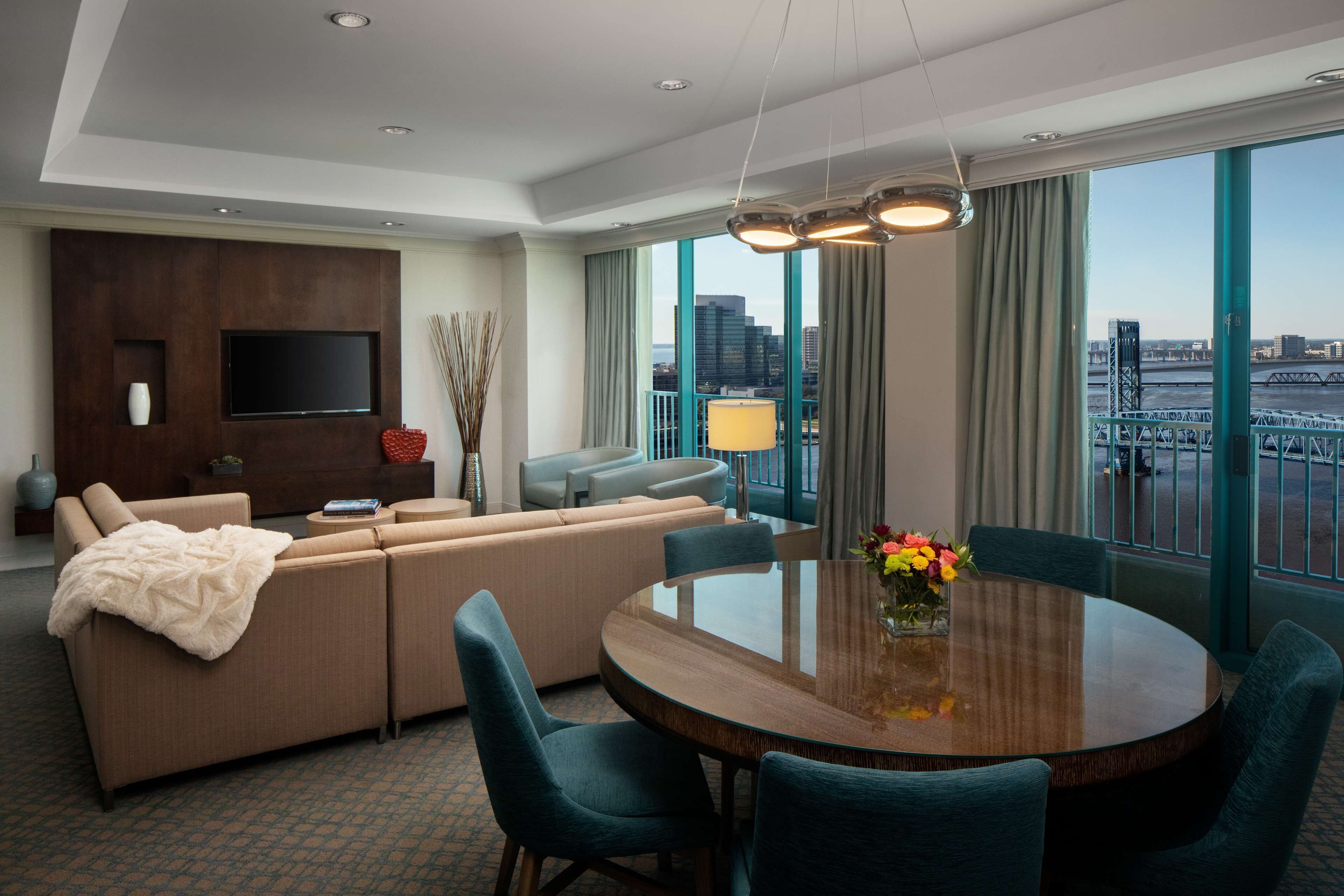 Ein modernes Hotelzimmer mit einer großen Couch, einem Esstisch und einem an der Wand montierten Fernseher.