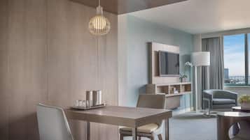 A modern hotel room with a dining area, a sofa, a TV, and a view of the city.