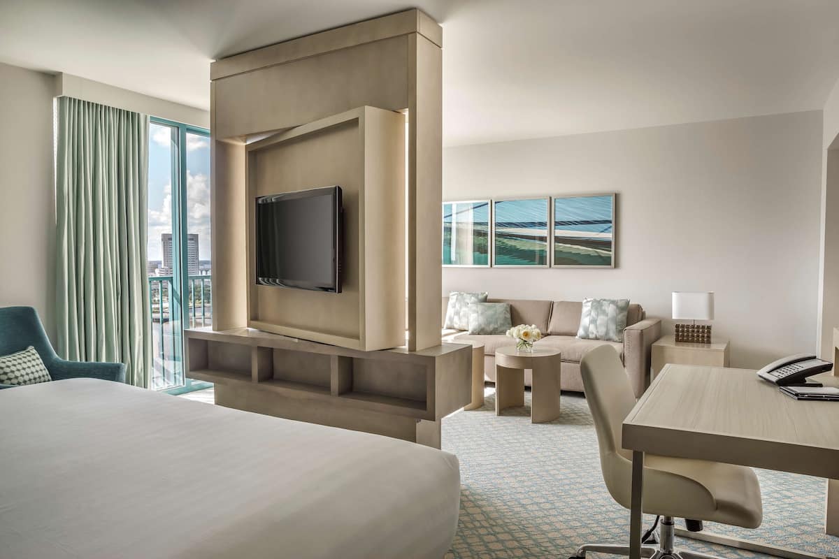 A hotel room with a large bed, a TV mounted on the wall, a sofa, a small table, and a desk with a phone.