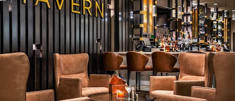 A modern bar area with leather chairs, a bar counter, and a wall with 'TAVERN' signage.