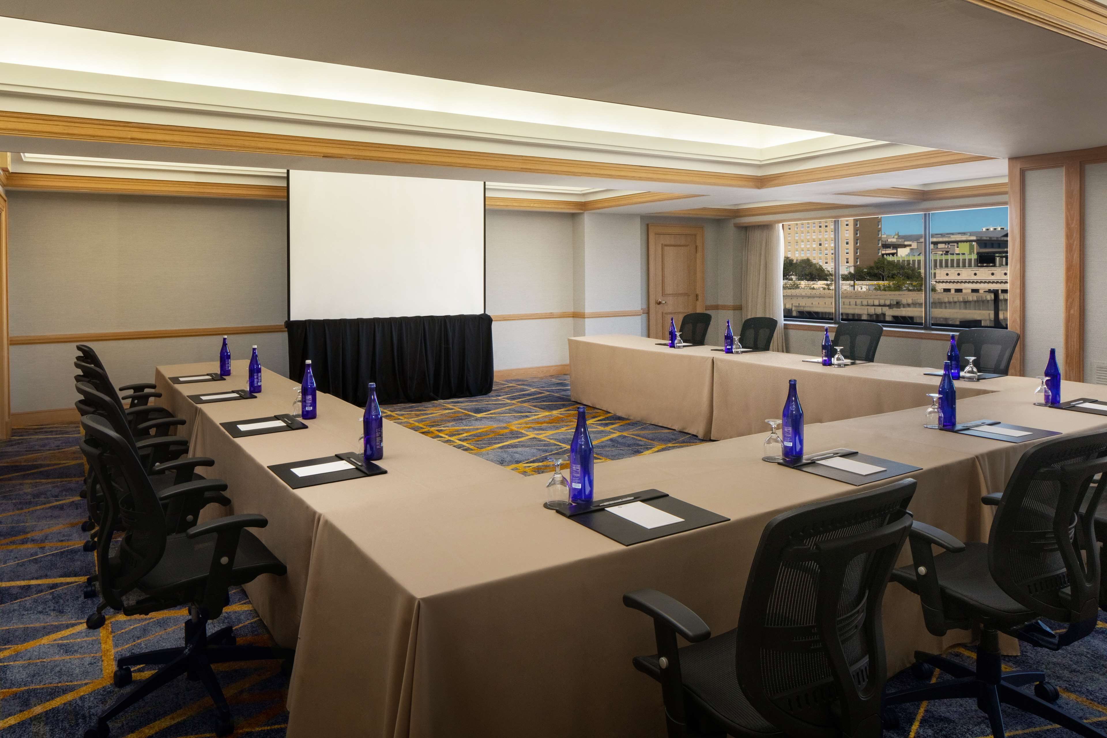 Un salón de conferencias con una larga mesa, sillas y una pantalla de proyector.