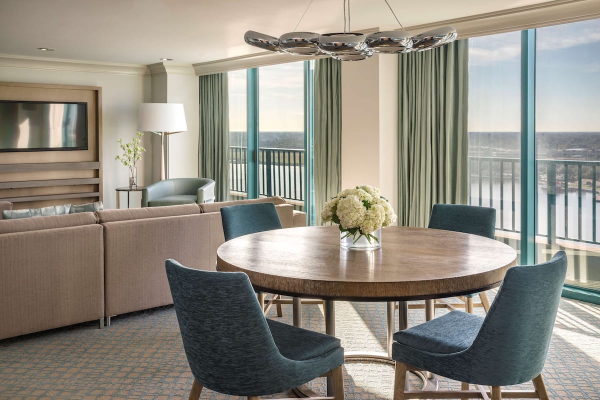 A modern hotel room with a large balcony, a round dining table, and a sofa.