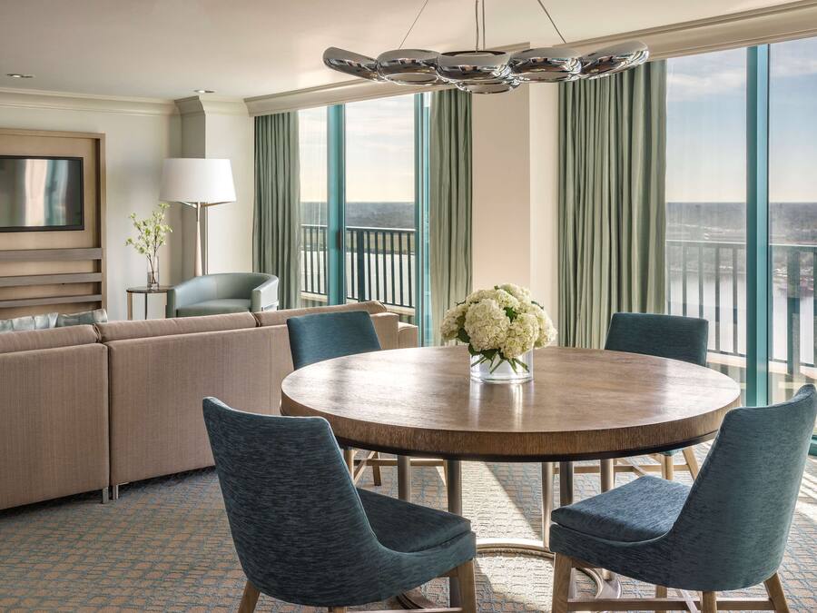 A modern hotel room with a large balcony, a round dining table, and a sofa.
