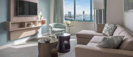 Une chambre d’hôtel moderne dotée d’une grande fenêtre, d’un téléviseur à écran plat, d’un canapé, d’un fauteuil et d’une petite table.