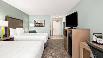 A hotel room with two beds, a desk with a coffee machine, a TV, and a picture on the wall.