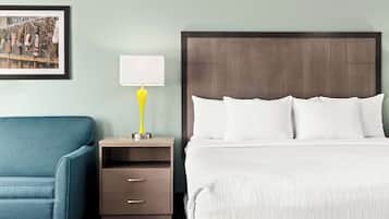 A hotel room with a bed, a blue sofa, a nightstand with a lamp, and a framed picture on the wall.