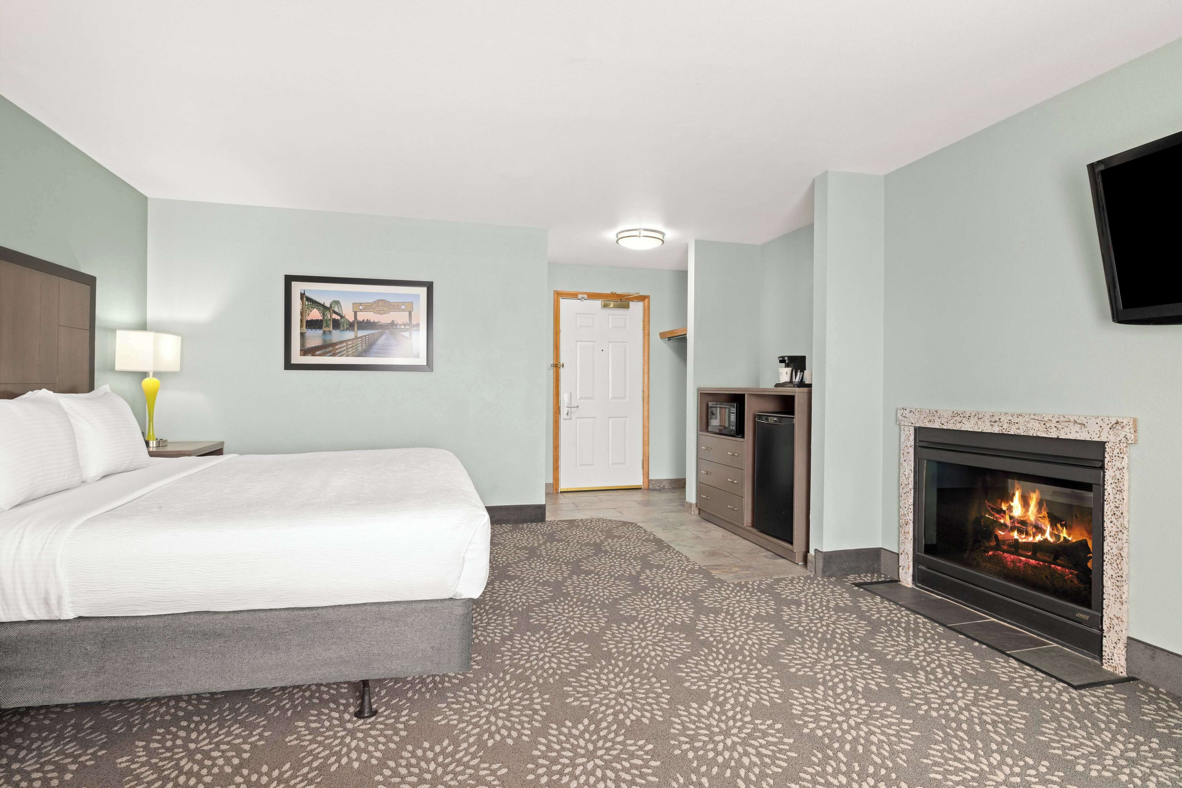 A hotel room with a bed, a television, a fireplace, and a door leading to another room.