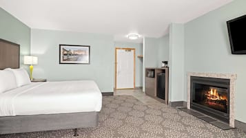A hotel room with a bed, a television, a fireplace, and a door leading to another room.
