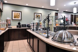 A breakfast bar with a microwave, toaster, and coffee machine. There are framed artworks on the wall and a glass partition separating the bar from the dining area.