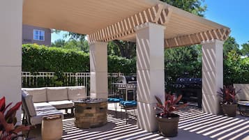 An outdoor patio with a pergola, seating, a barbecue grill, and potted plants.
