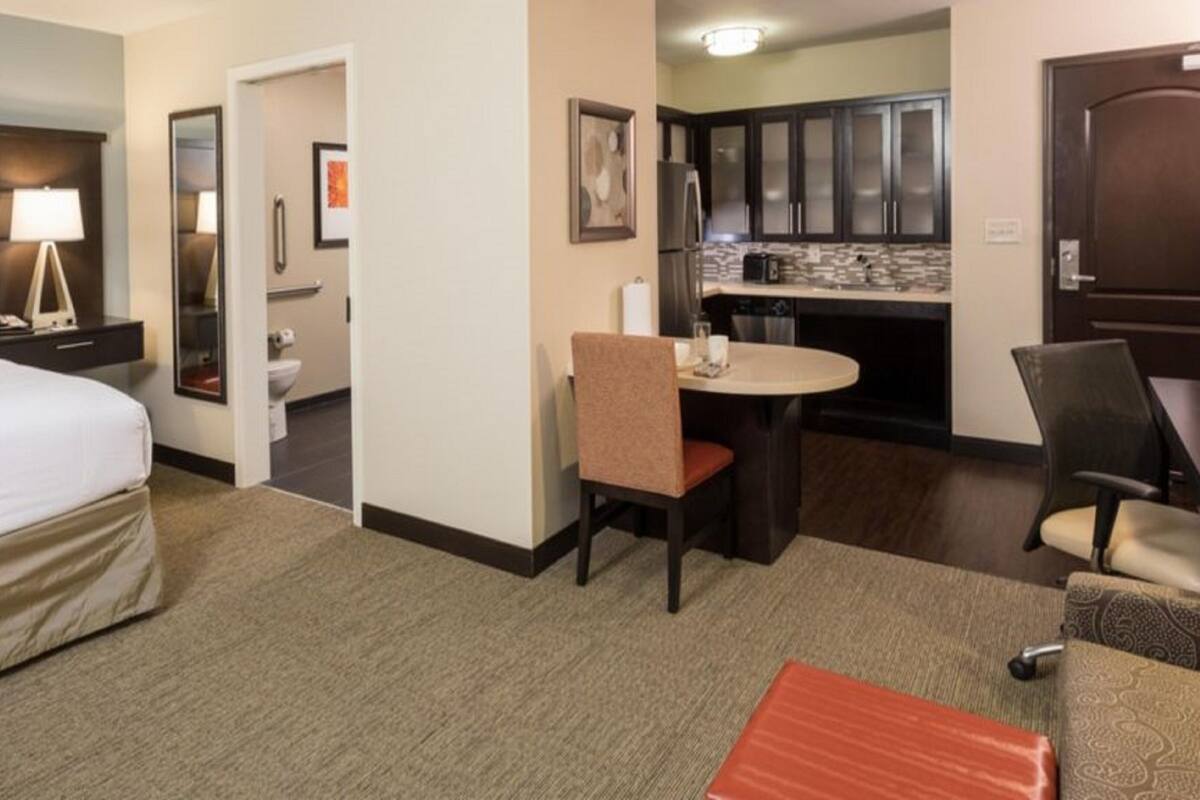 Een hotelkamer met een bed, een bureau, een stoel, een tafeltje en een kitchenette.