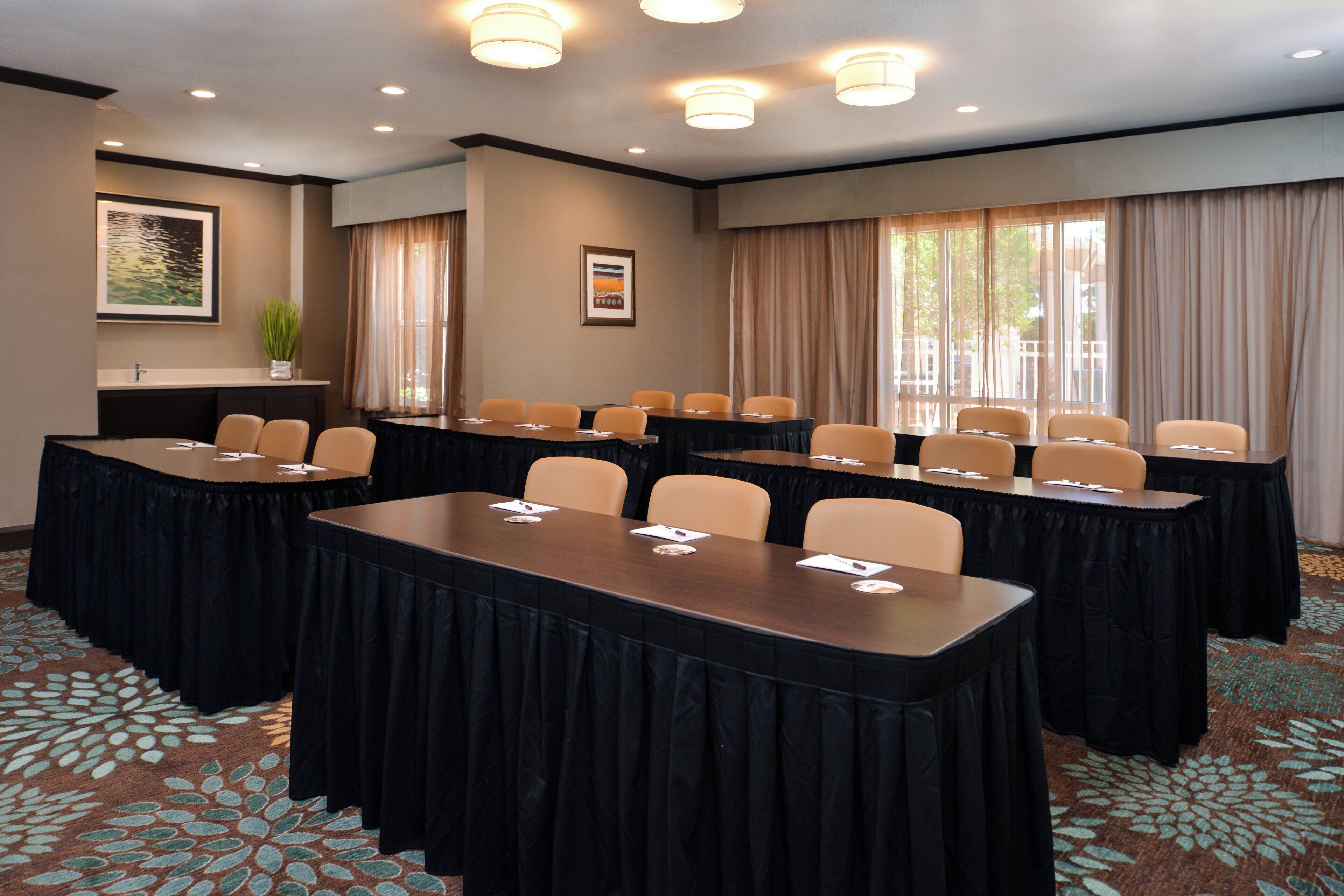 A conference room with multiple tables and chairs, a large window with curtains, and a framed picture on the wall.