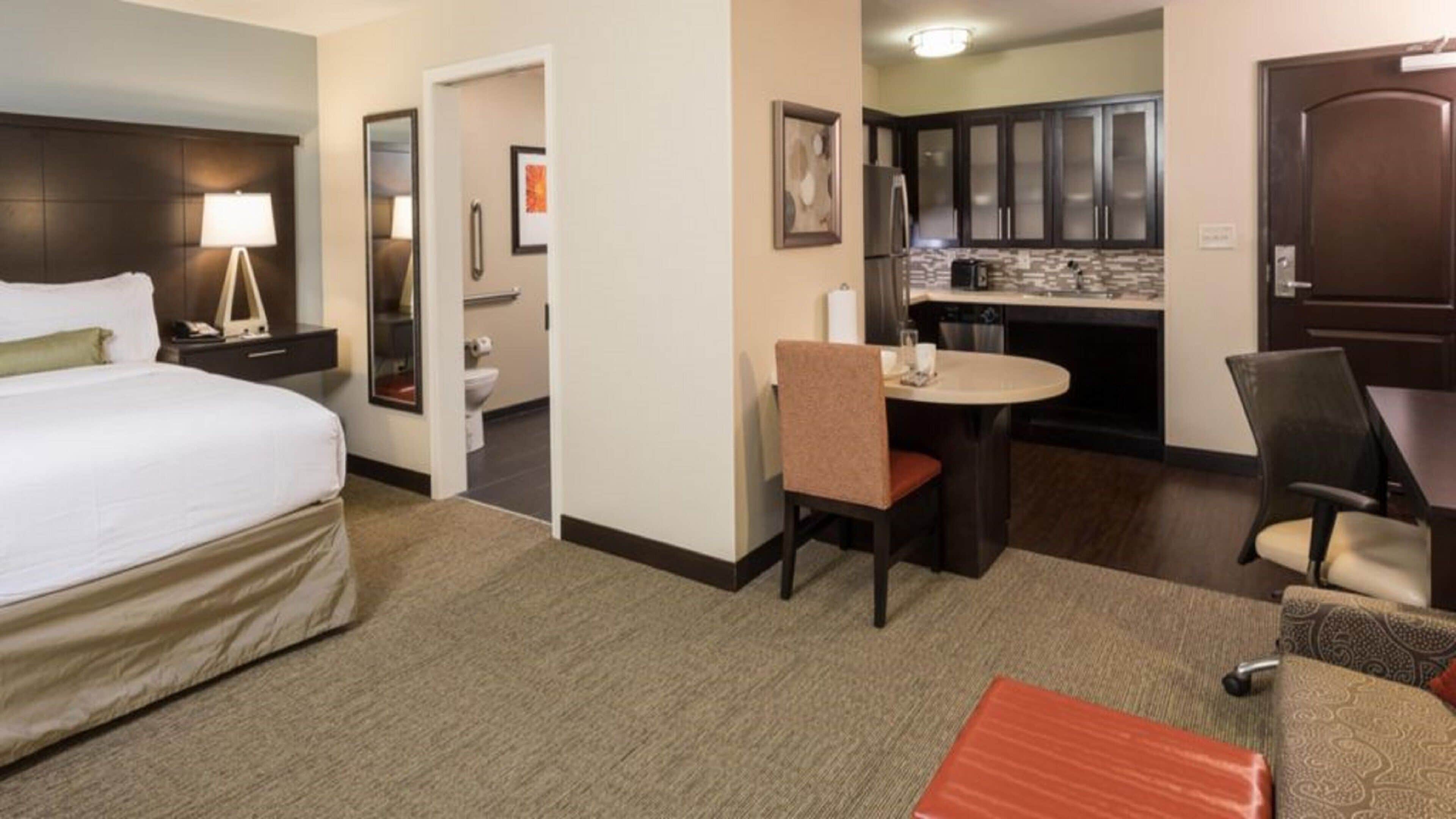 Habitación de hotel con cama, escritorio, silla, una mesita, kitchenette y baño.