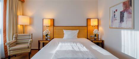 A hotel room with a large bed, two bedside lamps, a chair, and a painting on the wall.