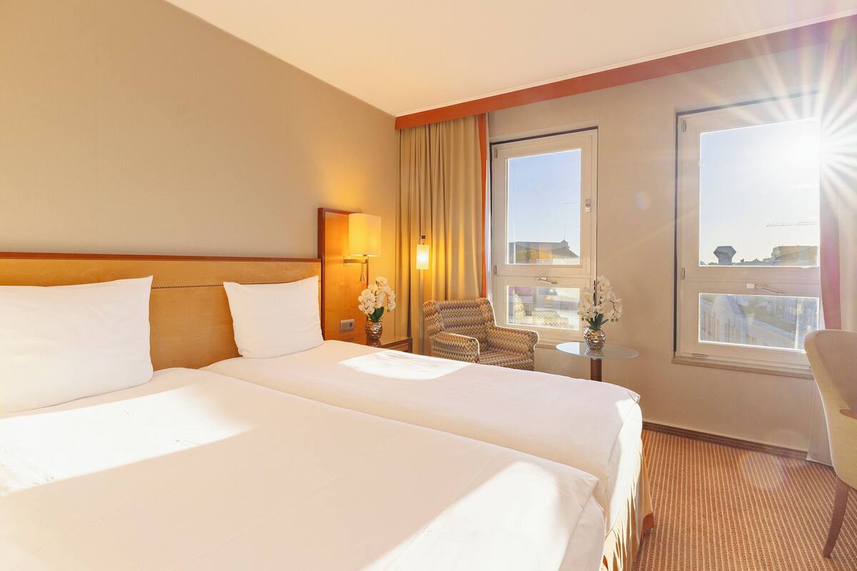Een hotelkamer met twee bedden, een stoel, een tafeltje en een raam met gordijnen.