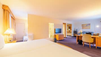A hotel room with a large bed, a desk, a chair, a television, and a small bathroom.