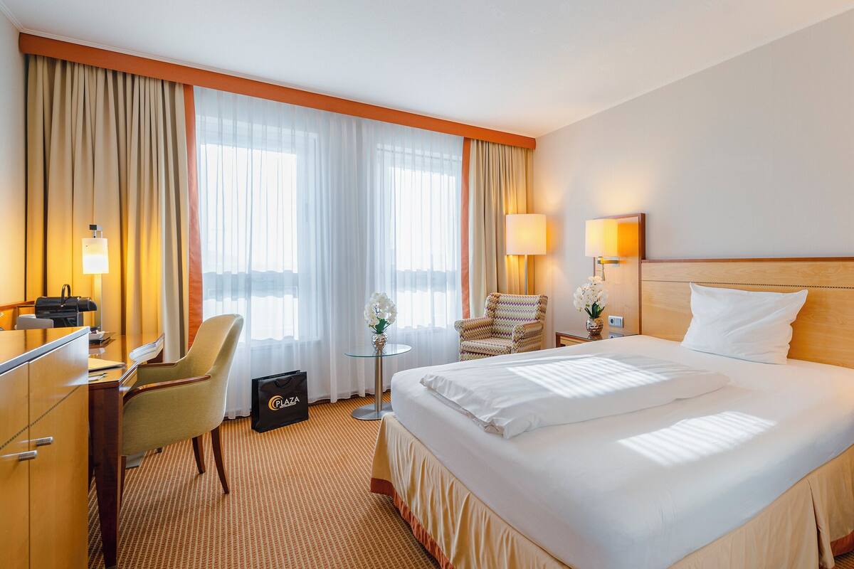 Een hotelkamer met een groot bed, een bureau, een stoel en een kleine tafel met een lamp en bloemen.