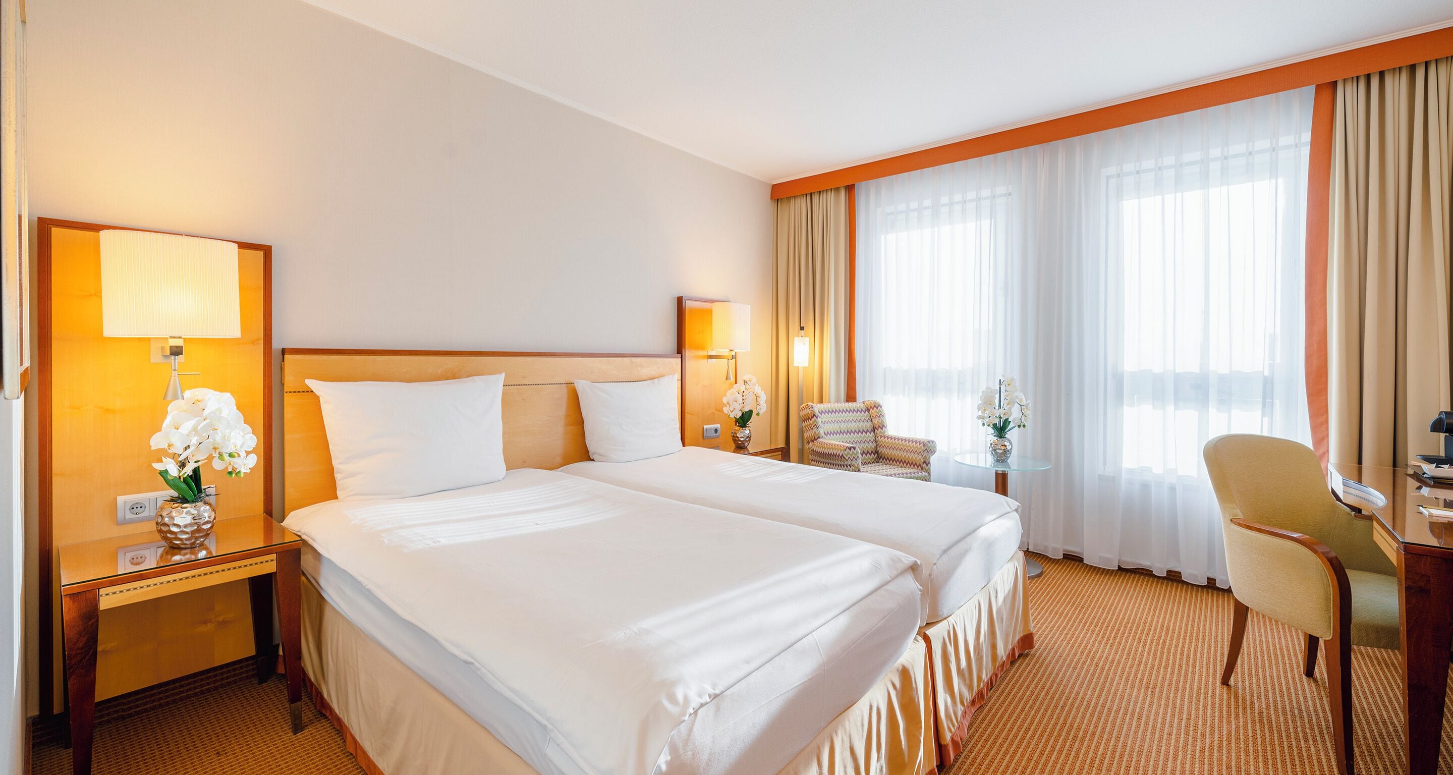 A hotel room with two beds, a desk, a chair, and a window with curtains.