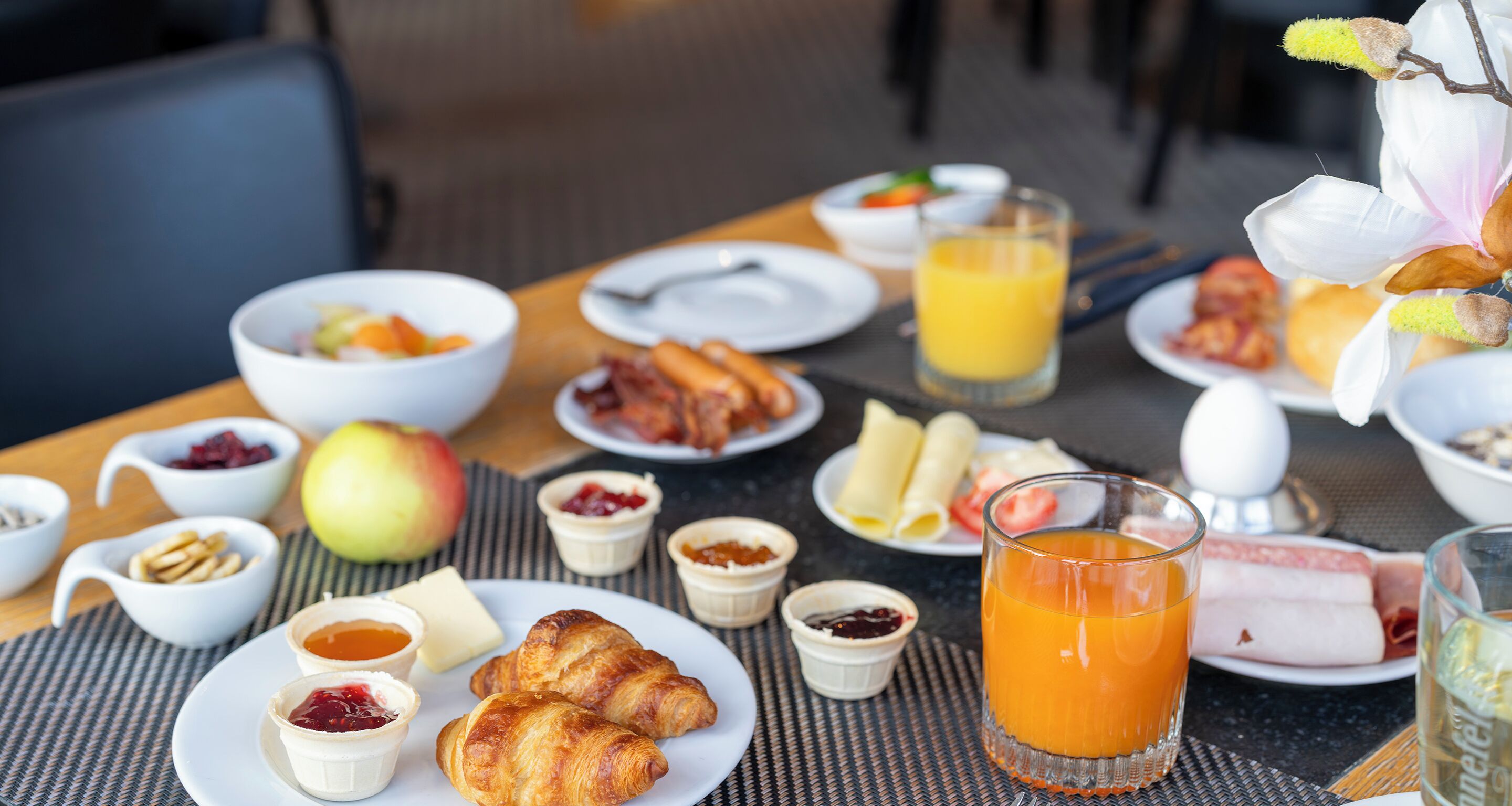 A breakfast table with croissants, eggs, bacon, fruit, and juice.