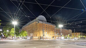 A modern building with a prominent dome and multiple floors, surrounded by a well-lit urban street at night.