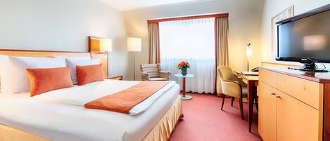 A hotel room with a large bed, a desk, a chair, a television, and a window with curtains.