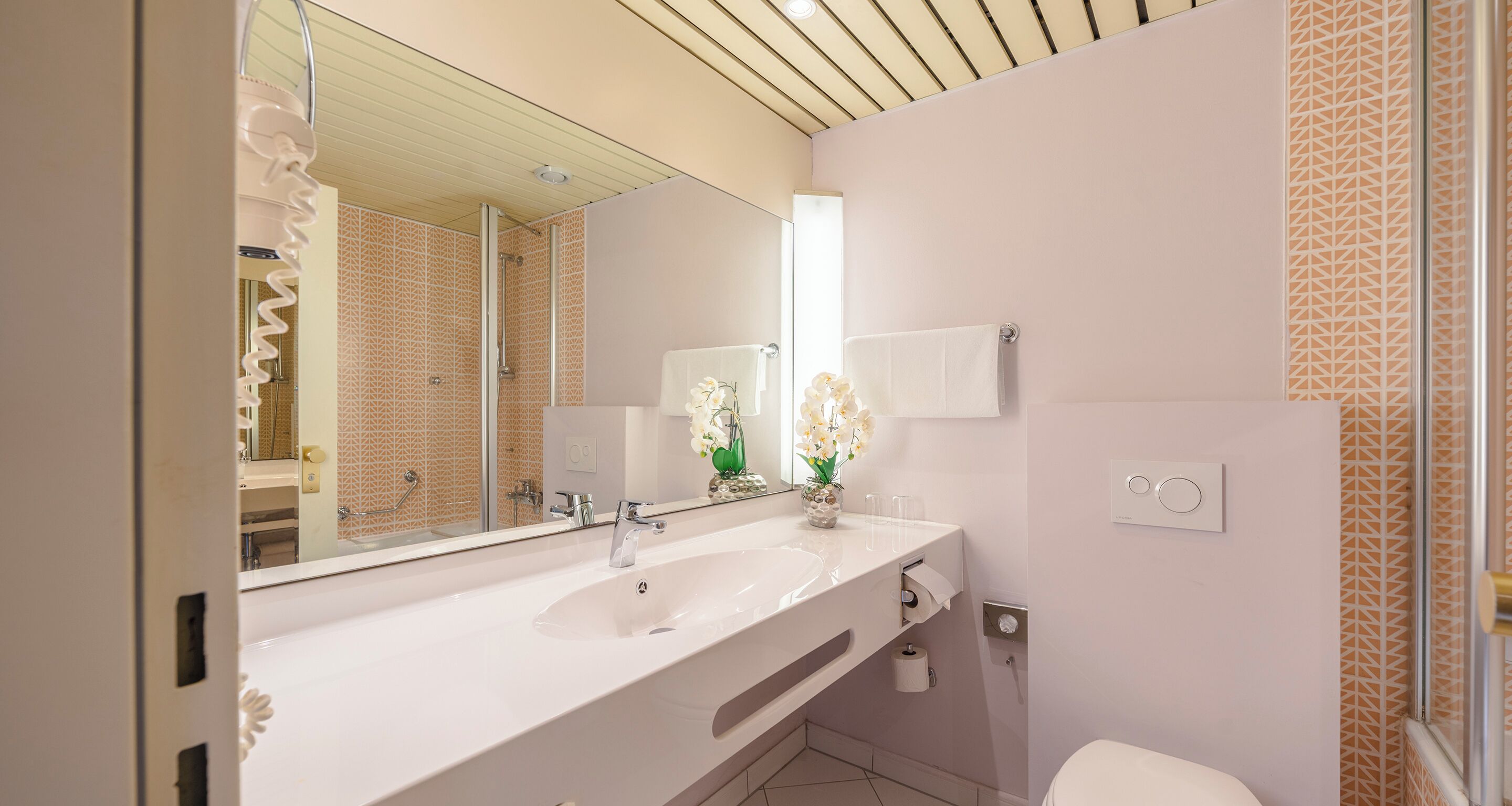 Un baño moderno con un espejo grande, un lavamanos blanco y un inodoro.