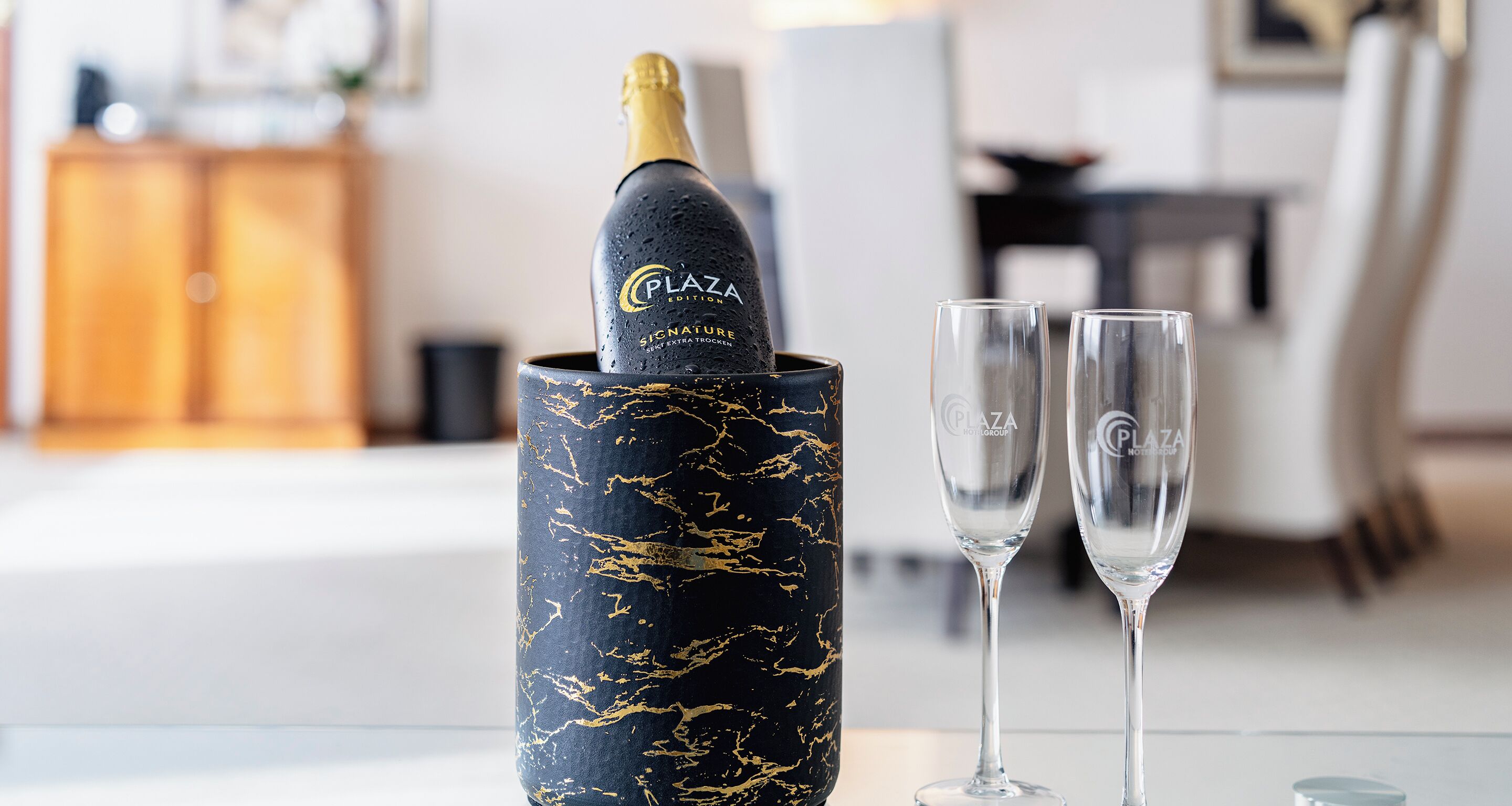 A bottle of champagne in a decorative holder with two glasses beside it.