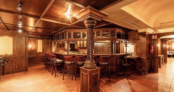 Una zona de bar con mobiliario de madera, una columna central y suelo de baldosas.