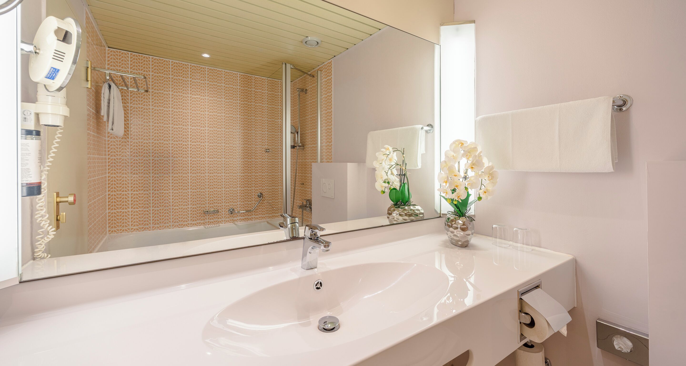 A bathroom with a white sink, a large mirror, a shower, and a towel rack.