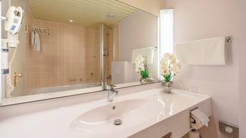 A bathroom with a white sink, a large mirror, a shower, and a towel rack.