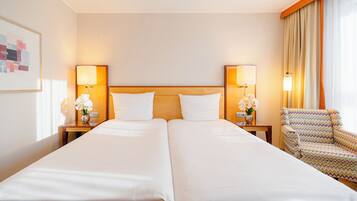 A hotel room with two beds, nightstands with lamps, a chair, and a wall-mounted artwork.