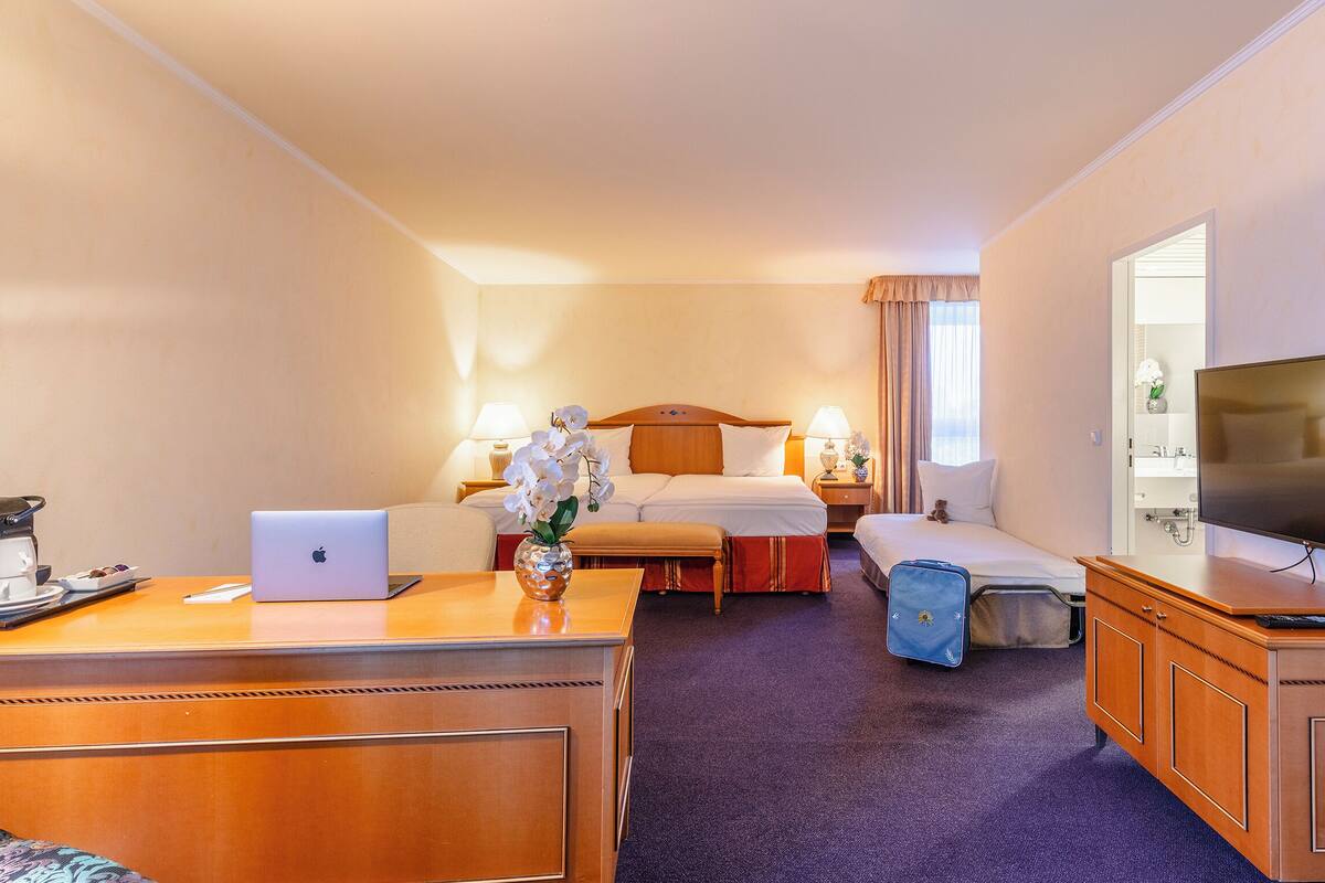 Een hotelkamer met een bed, een bureau met een laptop, een televisie en een kleine prullenbak.