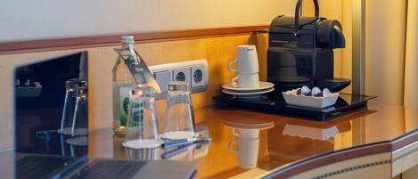 Ein Hotelzimmer mit einer Küchenzeile, einer Kaffeemaschine, einem Laptop und einem Glas Wasser auf der Arbeitsplatte.