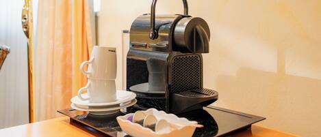 A coffee machine with a cup and saucer on a tray, a tissue box, and a small bowl of sugar cubes on a table.