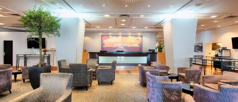 A hotel lobby with a reception desk, seating area, and a large chandelier.