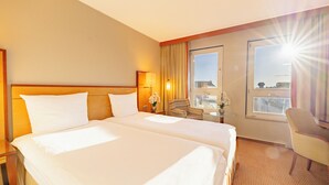 A hotel room with two beds, a sitting area with a chair, a small table, and a window with curtains.