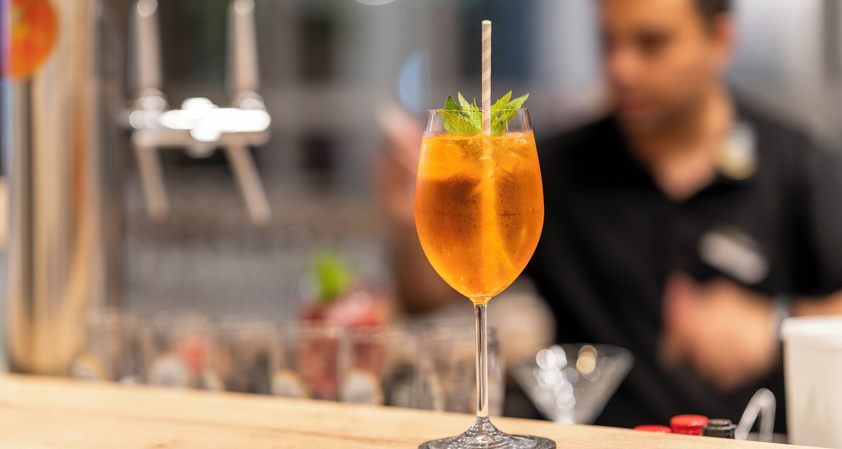 Un cocktail servi dans un verre avec une paille, décoré d’une feuille de menthe, posé sur le comptoir d’un bar.