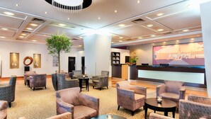 A spacious lobby with multiple seating areas, a large screen displaying a building, and a central column with a plant.