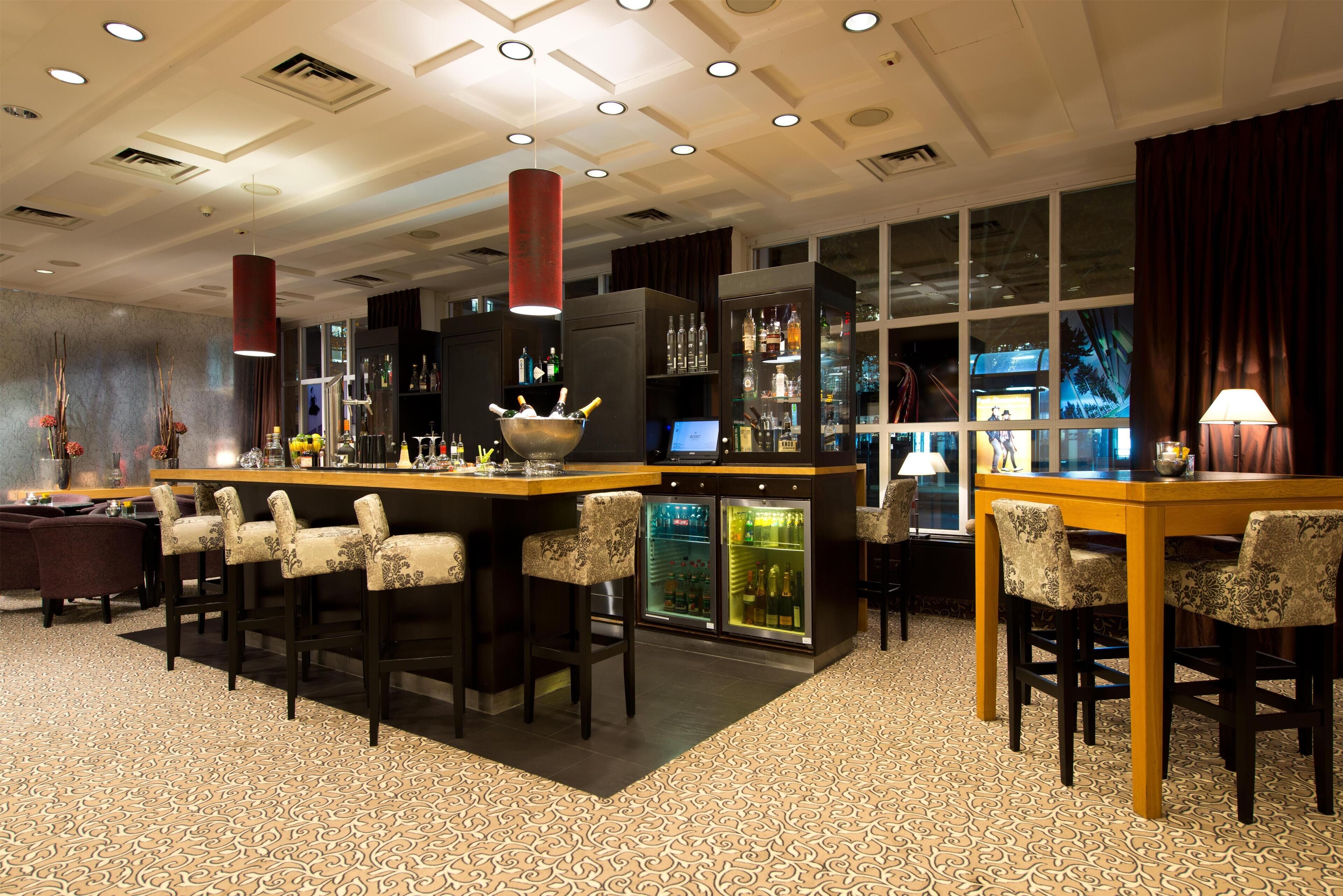 Zona de bar con barra, taburetes y refrigerador lleno de botellas.