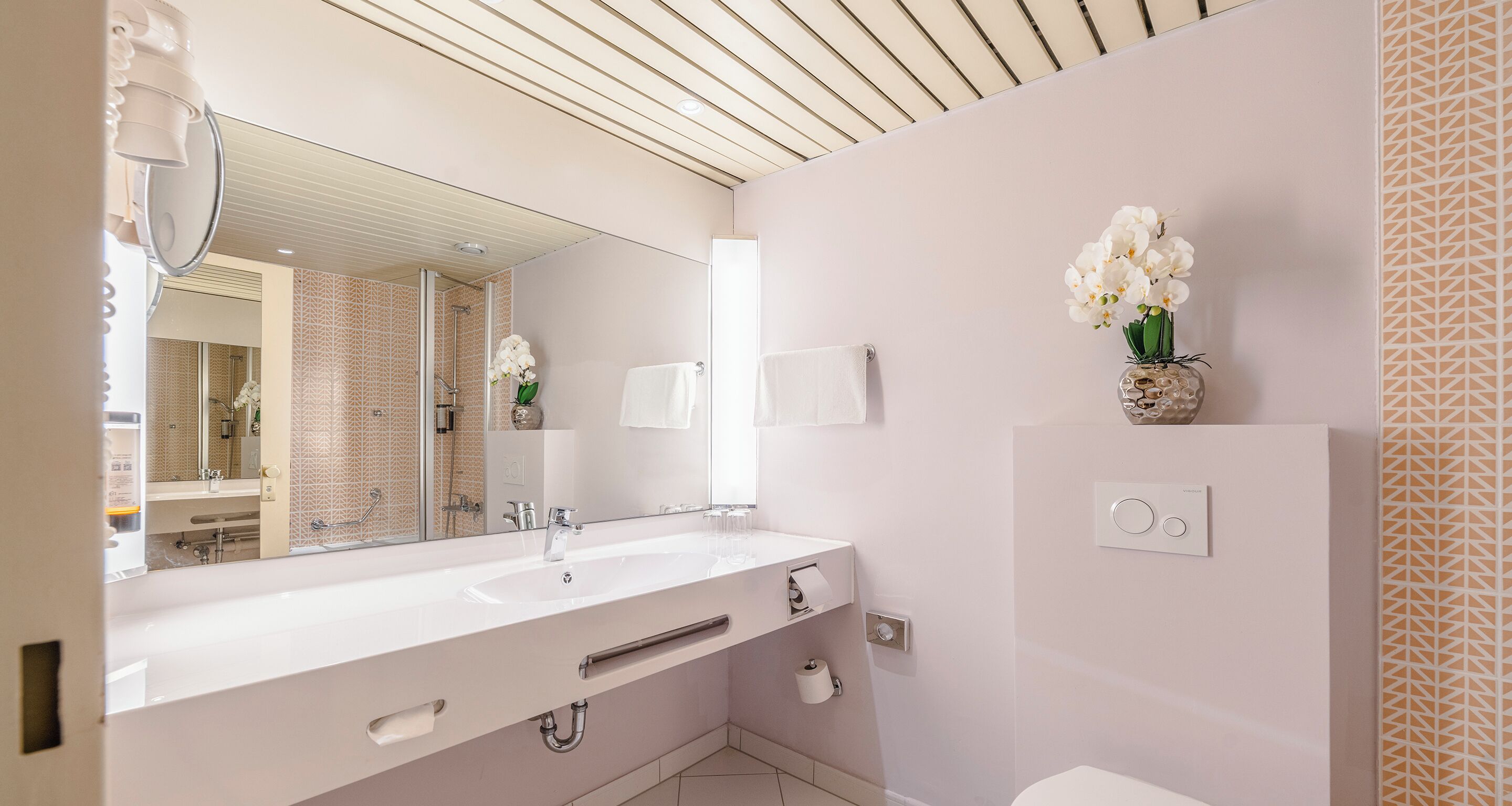 A modern bathroom with a large mirror, white sink, and a toilet.