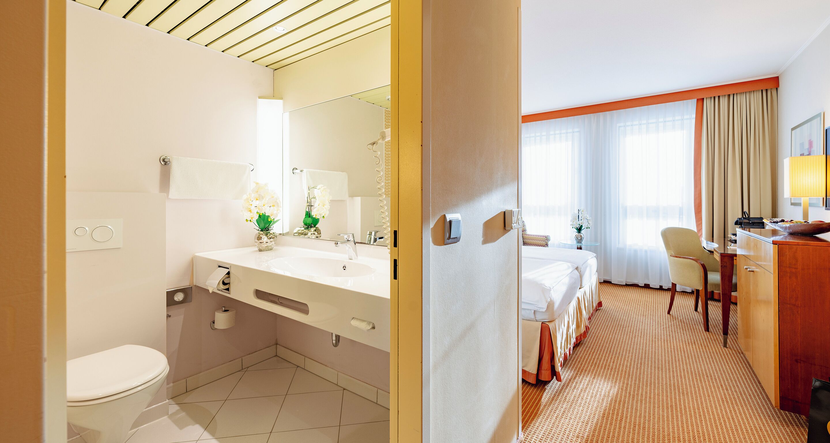 A hotel room with a bathroom, a bed, a desk, and a chair.