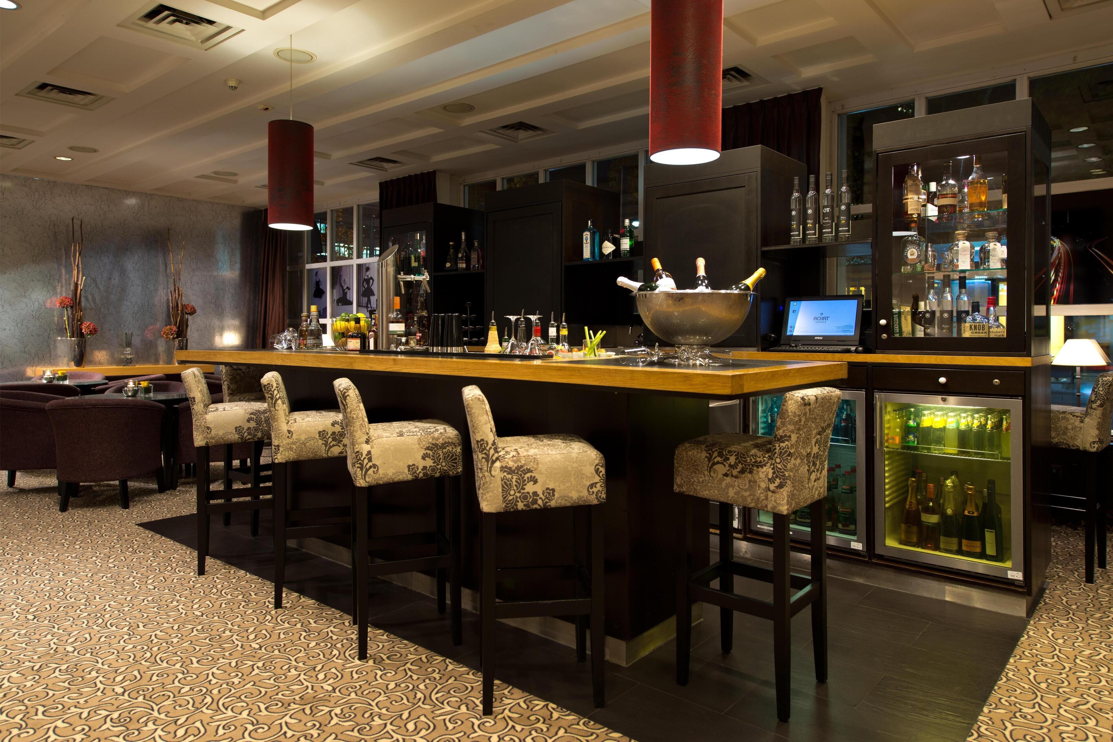 Un espace bar doté d’un long comptoir, de tabourets de bar, d’un grand saladier et d’un réfrigérateur rempli de bouteilles.