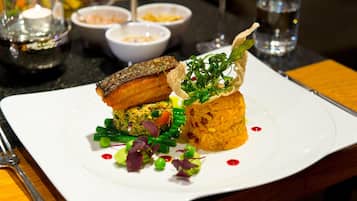 A white plate with a variety of food items including a piece of grilled meat, a vegetable patty, and a rice dish, accompanied by green beans and garnishes.
