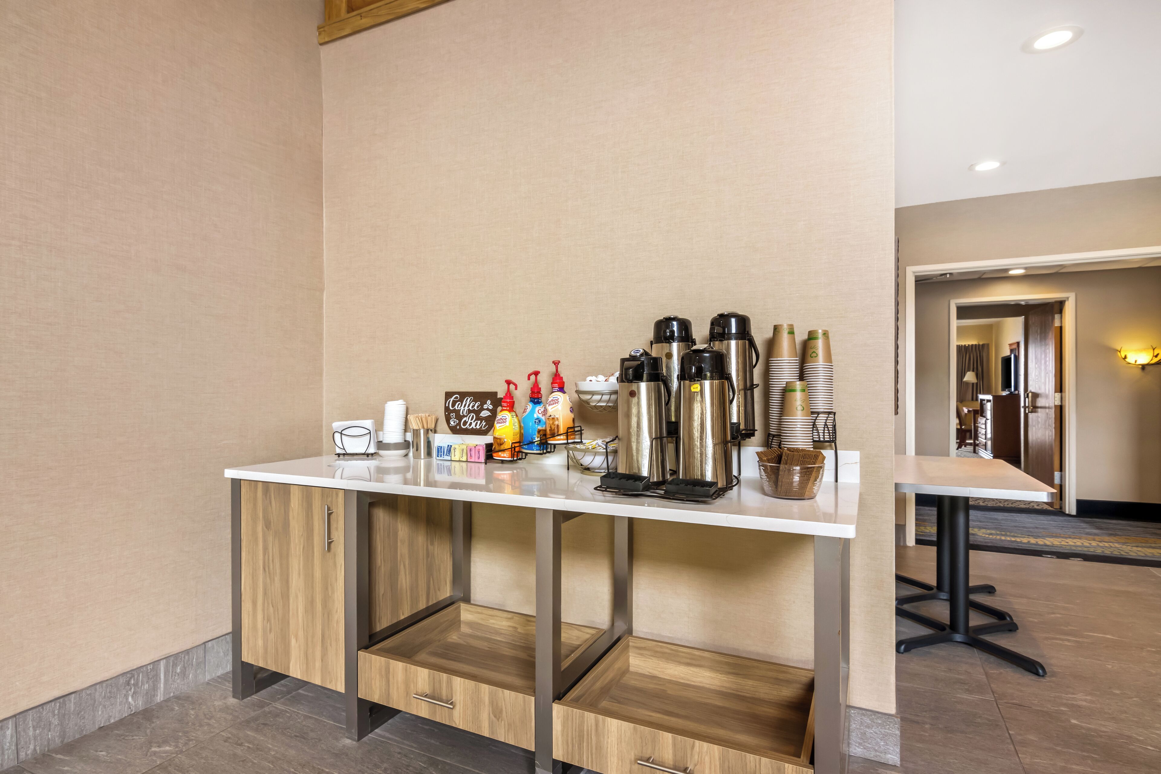 A hotel reception area with a white counter, coffee and tea station, and a seating area with a table and chairs.