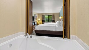 A hotel room with a large white bathtub, a double bed with white linens, and a desk with a chair.